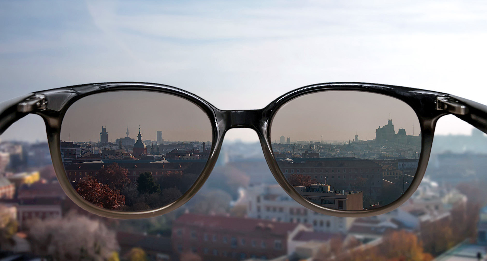 sluneční brýle držené před krajinou města v pozadí